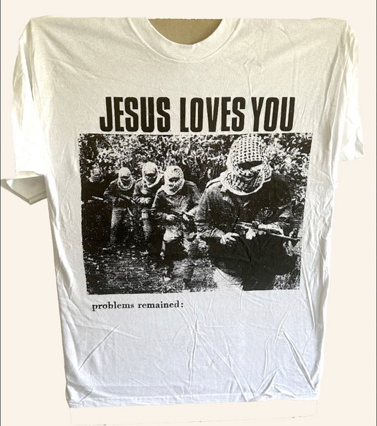 A white short-sleeve graphic t-shirt featuring a black and white photo print of  soldiers with the text 'JESUS LOVES YOU' above the image and 'problems remained:' below.
